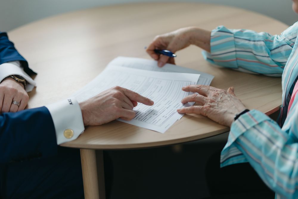Two people reviewing and signing a legal document at a wooden table in a professional meeting.