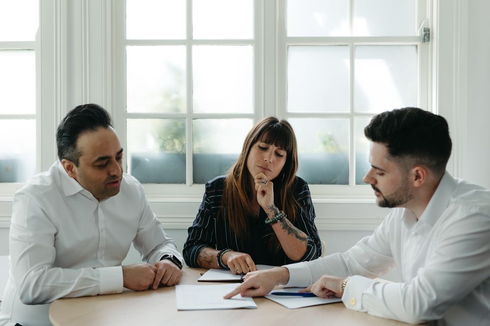 Three business professionals reviewing documents at a conference table in a bright modern office setting.