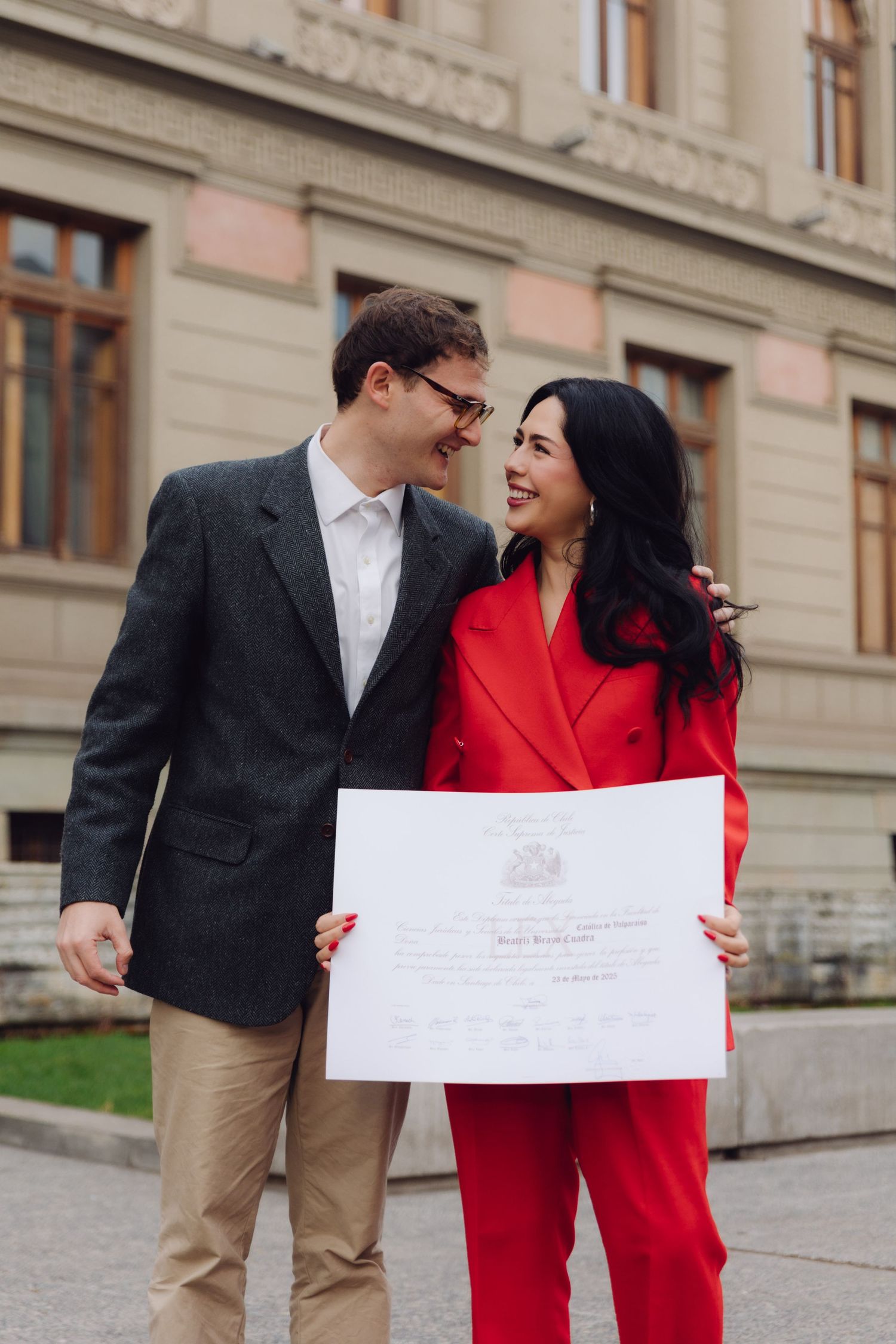 Couple laughing together while holding a certificate outside a university building.