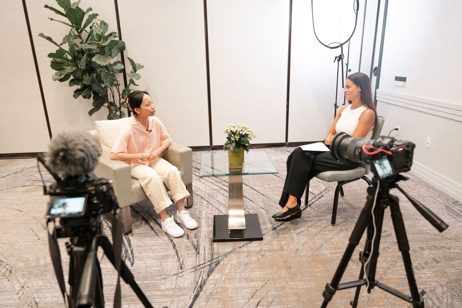 Two women sit facing each other in a professional video interview setup with cameras and studio lighting.