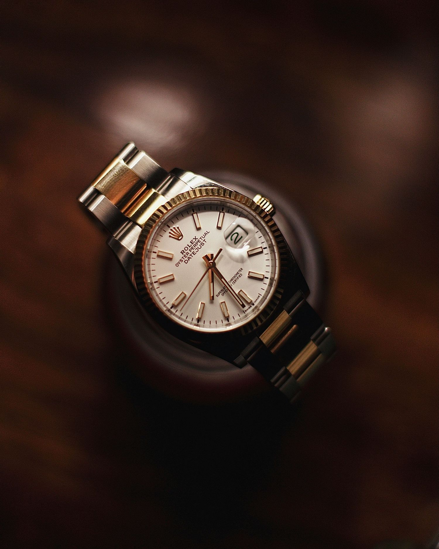 A luxury Rolex Datejust two-tone gold and silver watch with white dial on a dark brown background.