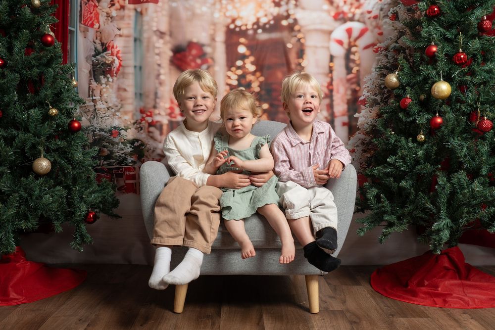 3 siblings sitting together on a chair and christmas backdrop