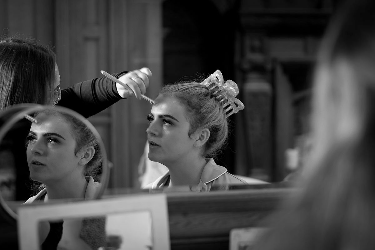 Black and white photo of a woman getting her hair styled with rollers by a hairstylist backstage.