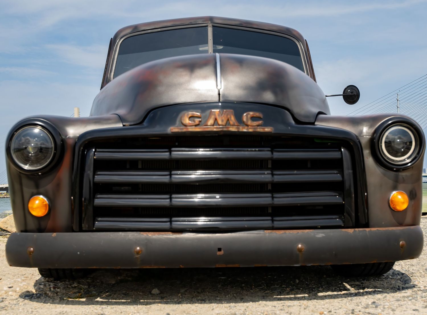 Vintage GMC truck front view showing classic chrome grille, round headlights, and patina rust finish on a sunny day.