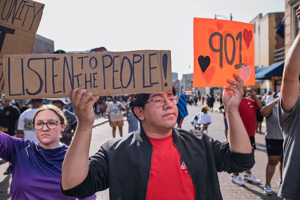 Protesters march holding signs reading Listen to the People and 901 at an outdoor demonstration.