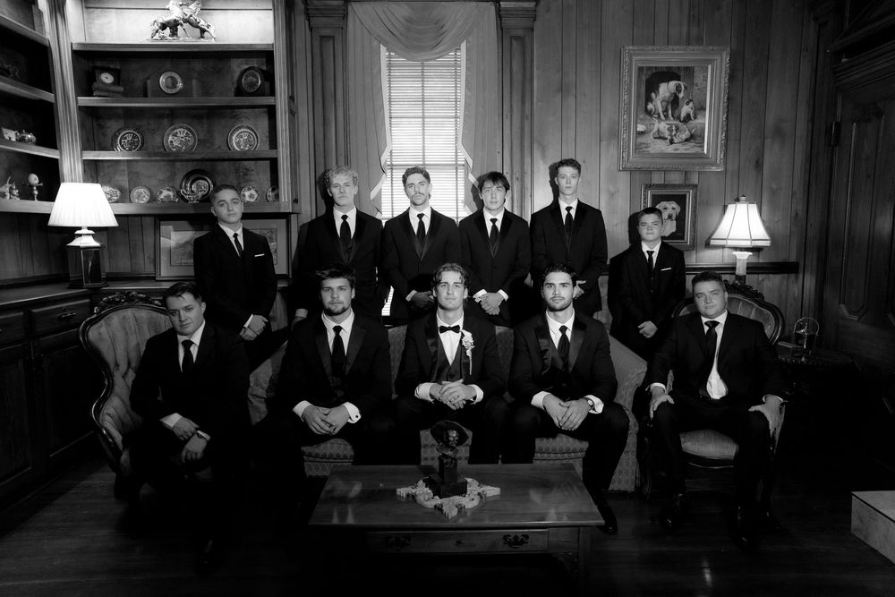 Black and white formal group portrait of twelve men in suits posed in an elegant wood-paneled room.