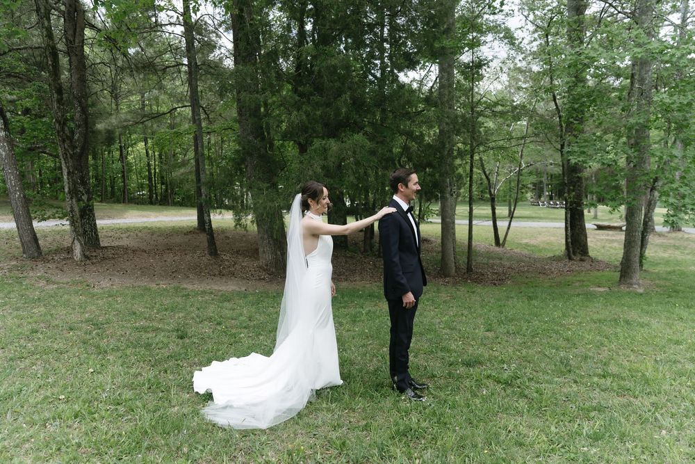 Bride and groom share a romantic first look moment in a lush green forest clearing during their outdoor wedding.