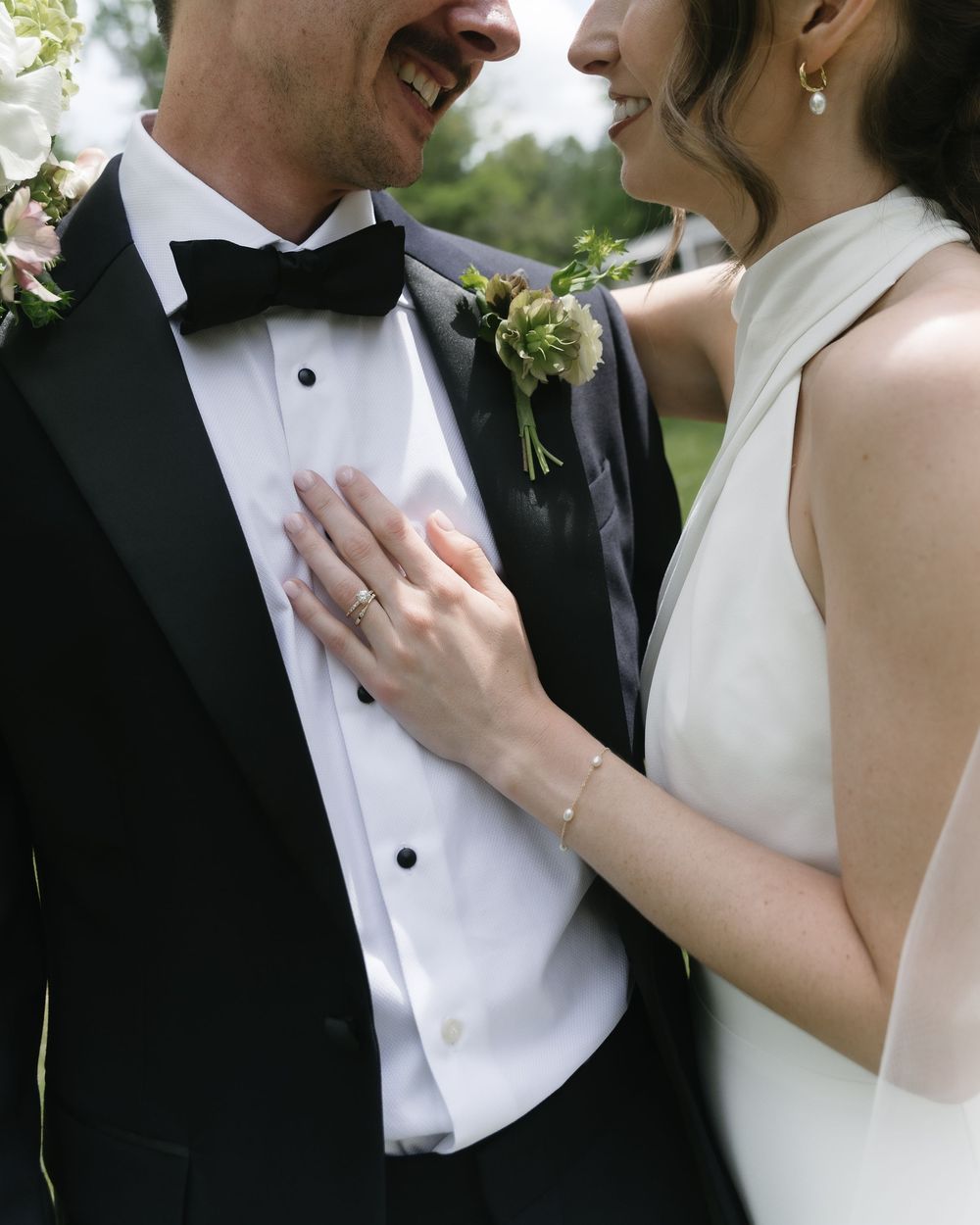 Bride and groom laughing together, bride wearing white halter gown with diamond ring, groom in black tuxedo with bow tie.
