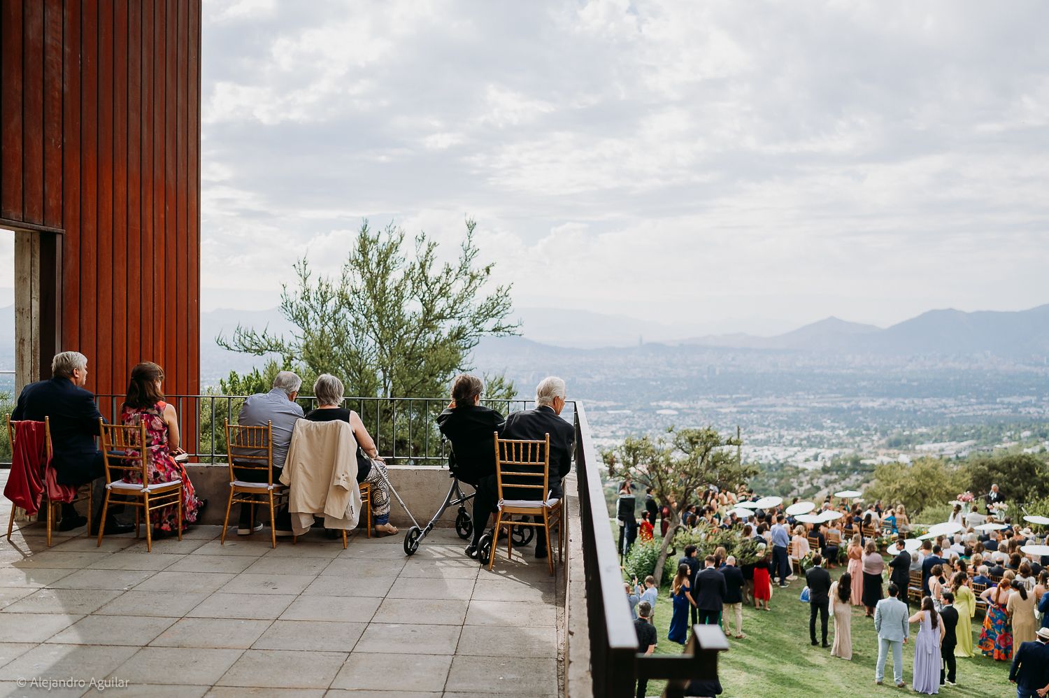 Wedding guests enjoy panoramic mountain valley views from elevated terrace venue with lush green landscape below.