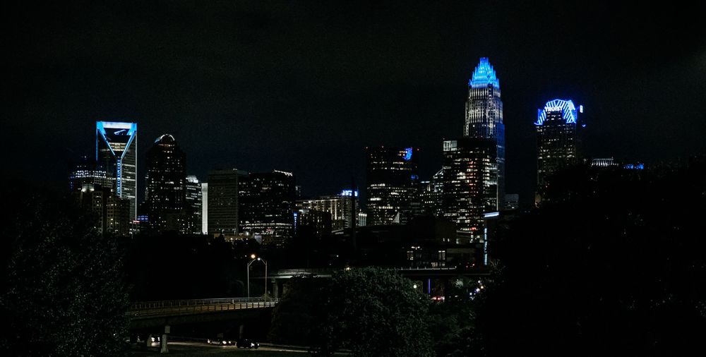 Charlotte, NC skyline at night with illuminated skyscrapers glowing blue against the dark sky.