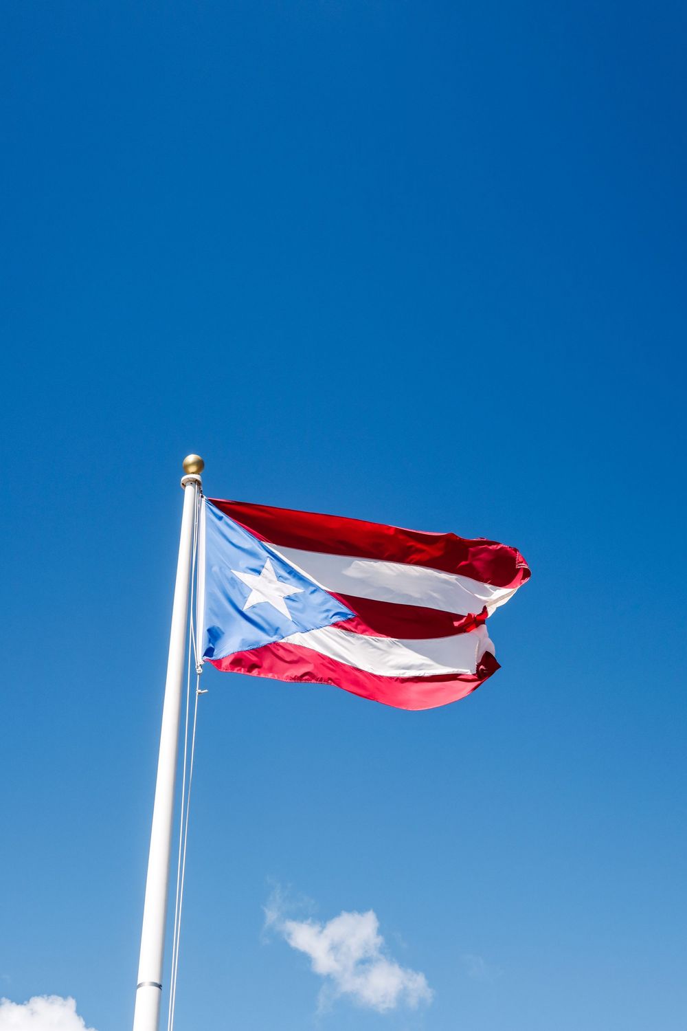 Puerto Rico flag waving in the wind against a bright blue sky on a white flagpole.