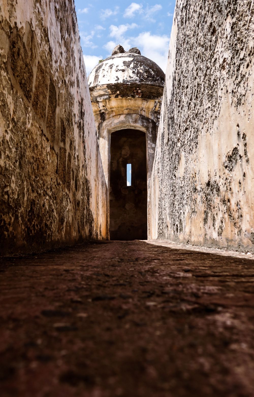Ancient stone fortress corridor leading to a weathered sentry box turret under blue sky at El Morro, Puerto Rico.