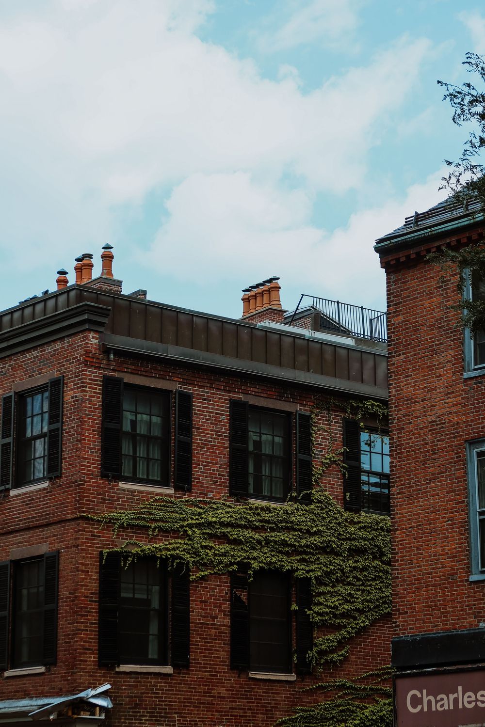 Red brick building with ivy-covered walls, black shuttered windows, rooftop chimneys, and a Charles Street sign under cloudy skies.