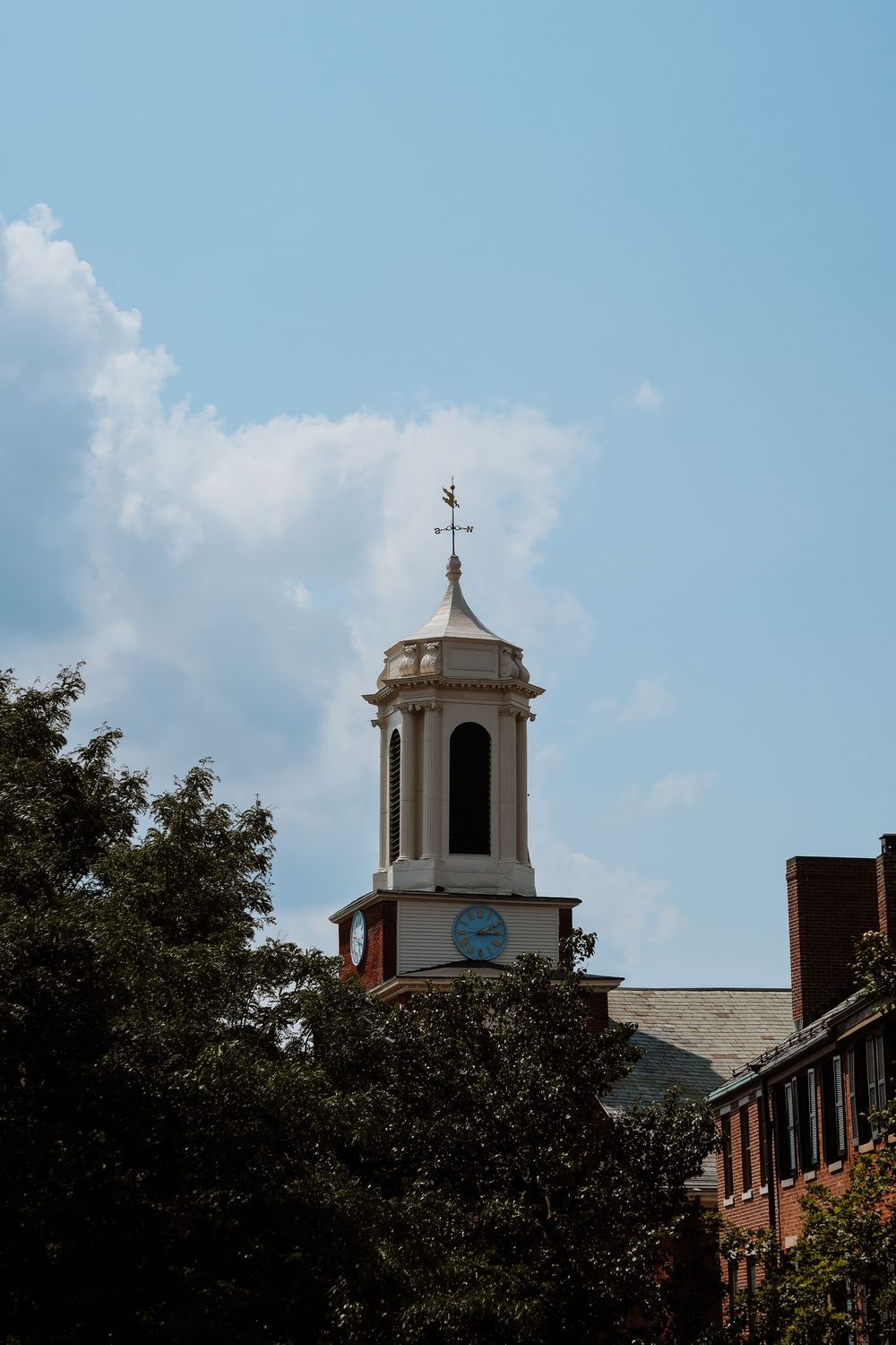 Historic brick building with white colonial cupola, clock tower, and weather vane against a blue sky.