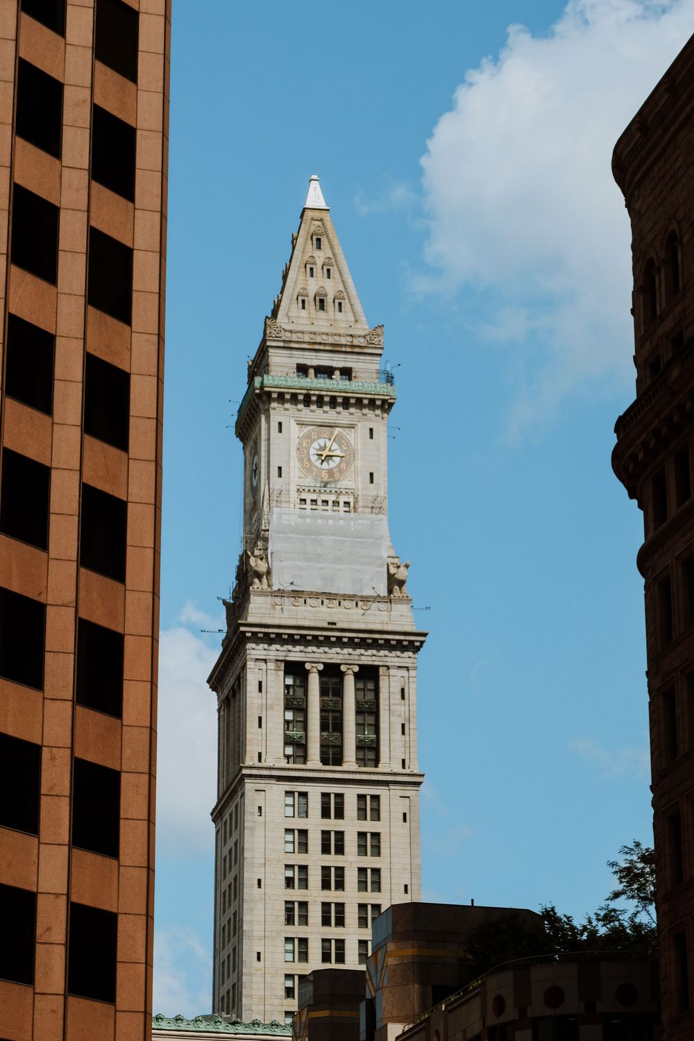 Boston Custom House Tower clock tower rises between modern buildings against a blue sky.
