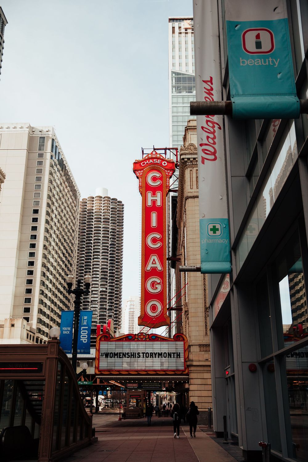 The iconic Chicago Theatre marquee sign lit up on State Street with Walgreens and city skyscrapers in the background.