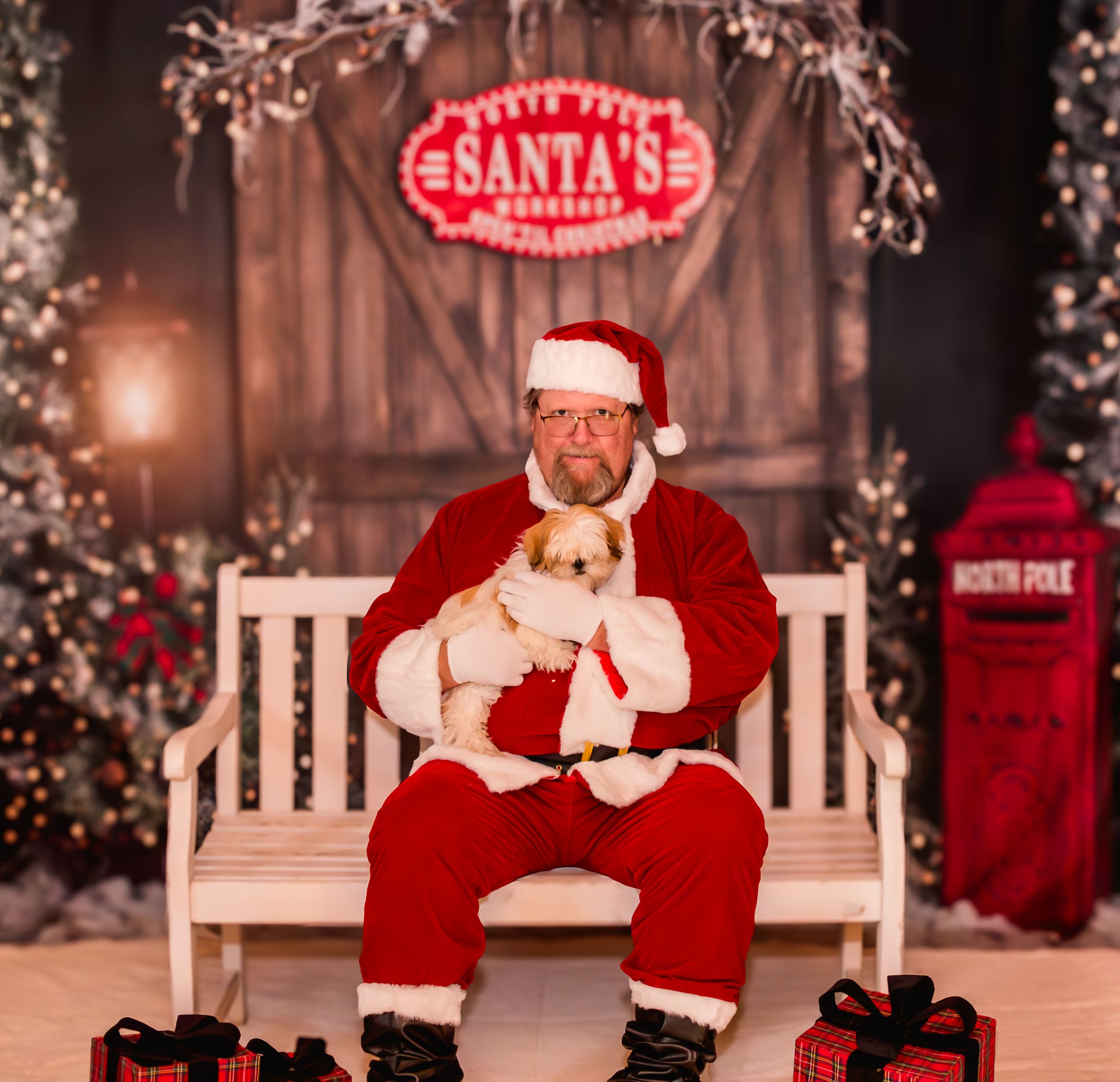 Two children sit with Santa Claus in his workshop, surrounded by festive Christmas decorations and trees.