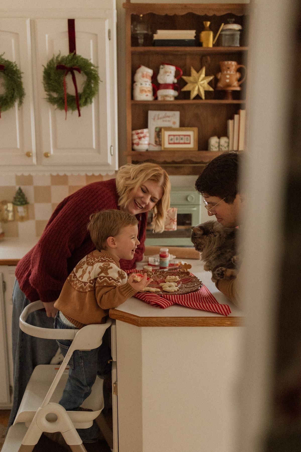 Family decorating Christmas cookies in a festive kitchen with holiday wreaths and seasonal decor.