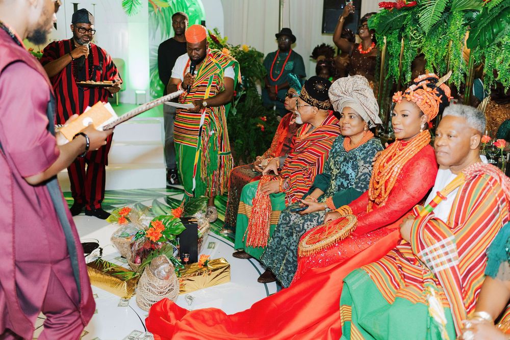 Traditional African wedding ceremony with guests in vibrant kente cloth and coral beads gathered for a cultural ritual.