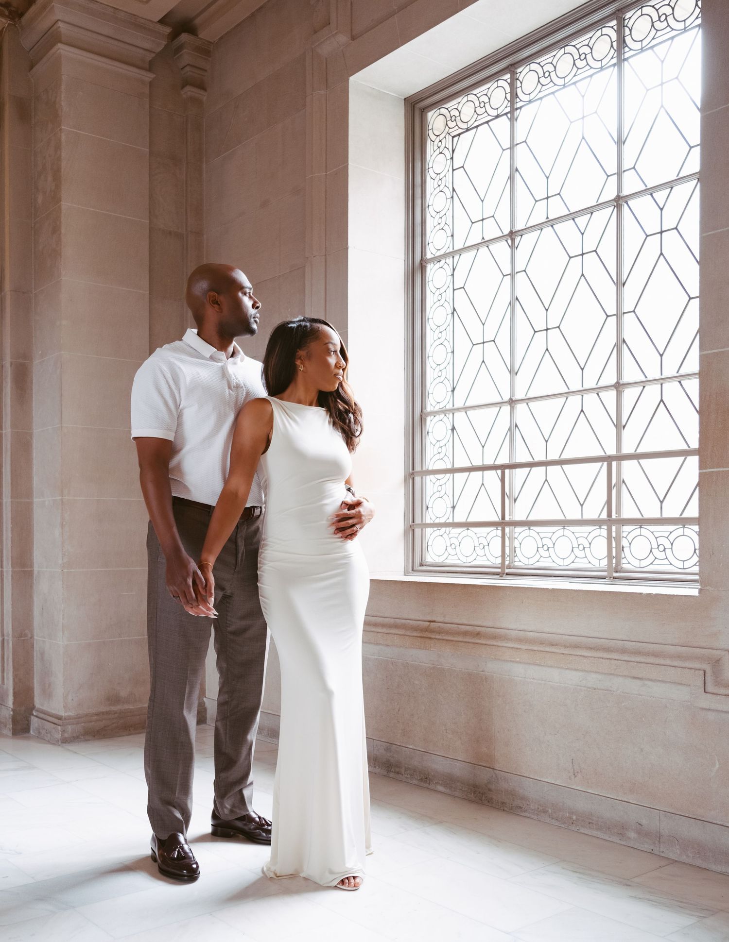 Couple holding hands in elegant domed rotunda with marble columns and arched window backdrop.