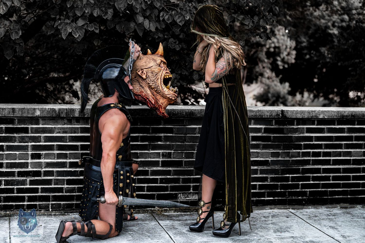 Black and white fantasy cosplay photo of gladiator kneeling before hooded figure. Chi.Shooters meet tonybrettman tattoo_jessie