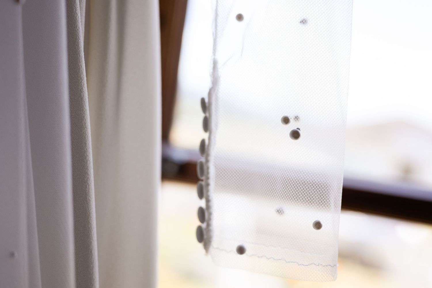 Close-up of a white perforated plastic strip attached to a curtain panel near a window frame.