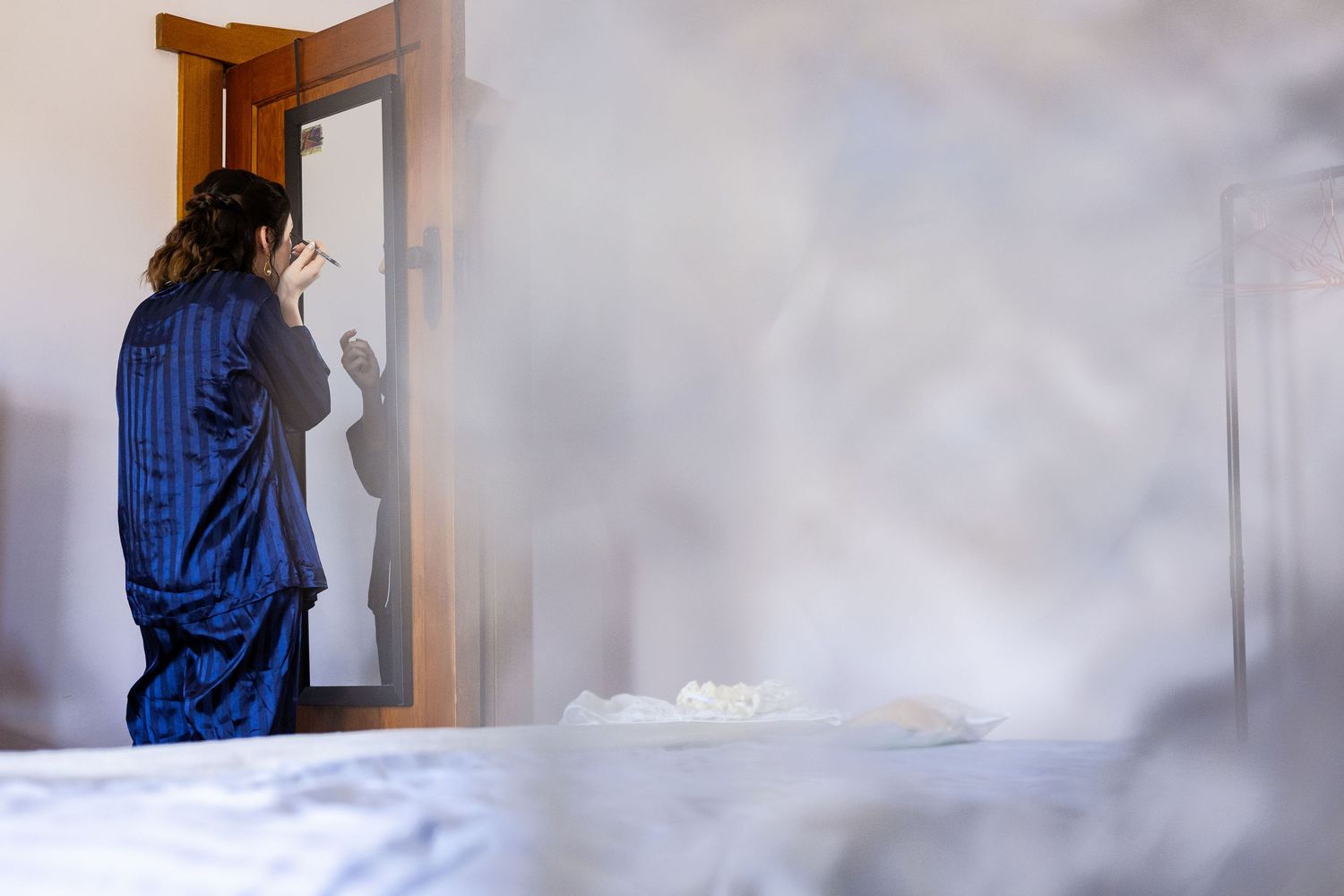 Person in blue striped pajamas smoking a cigarette by a doorway in a smoky bedroom.