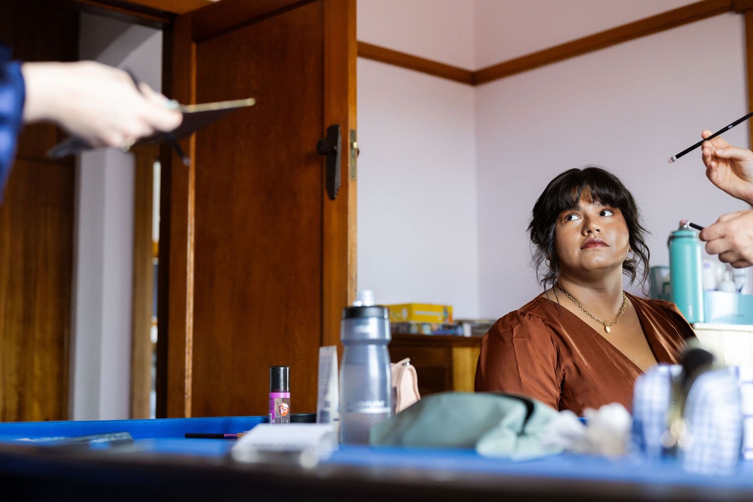 Person sitting at a vanity table getting makeup applied in a cozy room with beauty products.