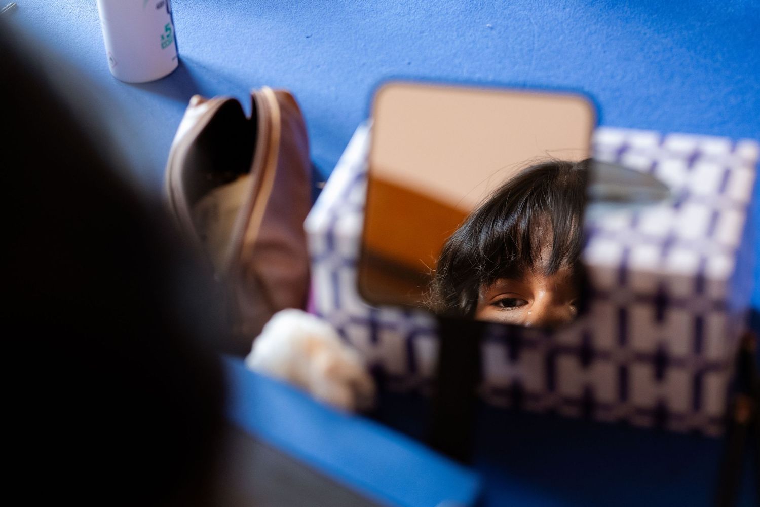 Child's reflection visible in a small mirror on a blue patterned surface, capturing a candid moment.