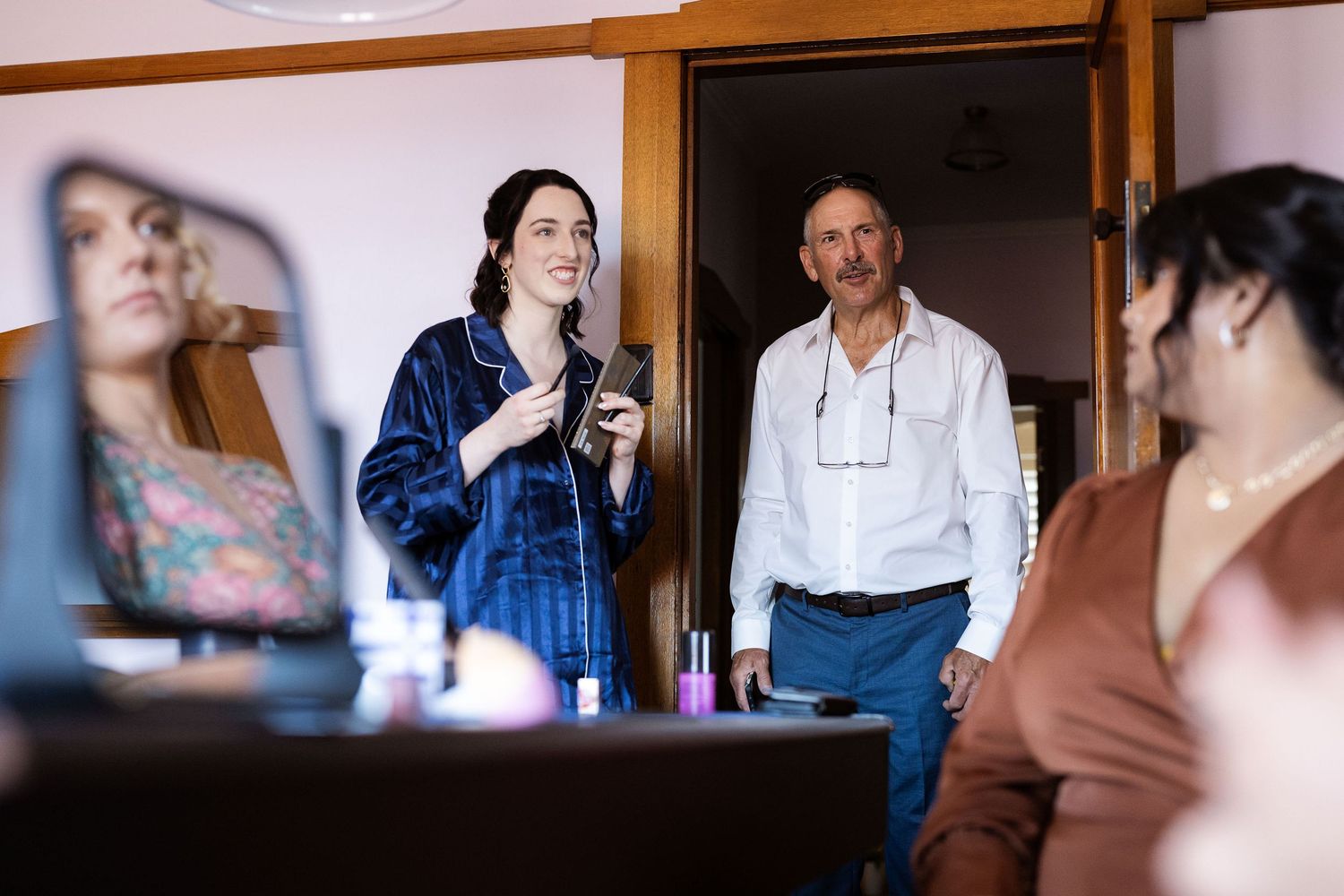 Bride in blue robe laughing with guests during wedding morning preparations indoors.