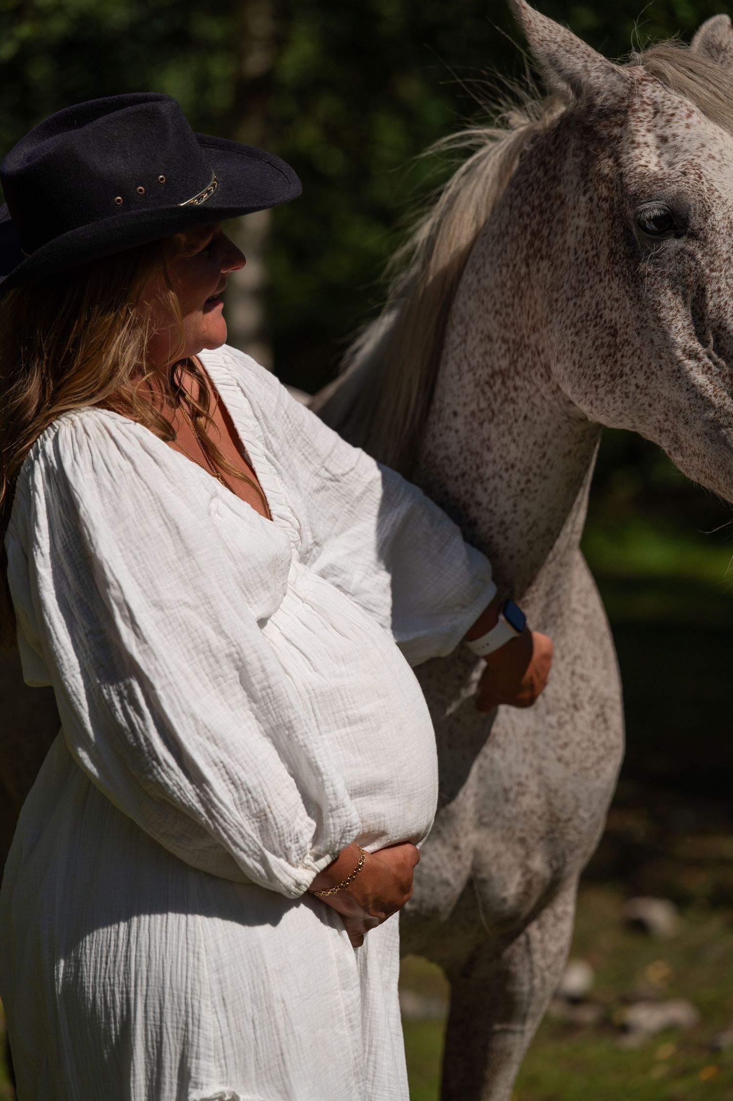 Pregnant woman in white dress and cowboy hat with grey horse.