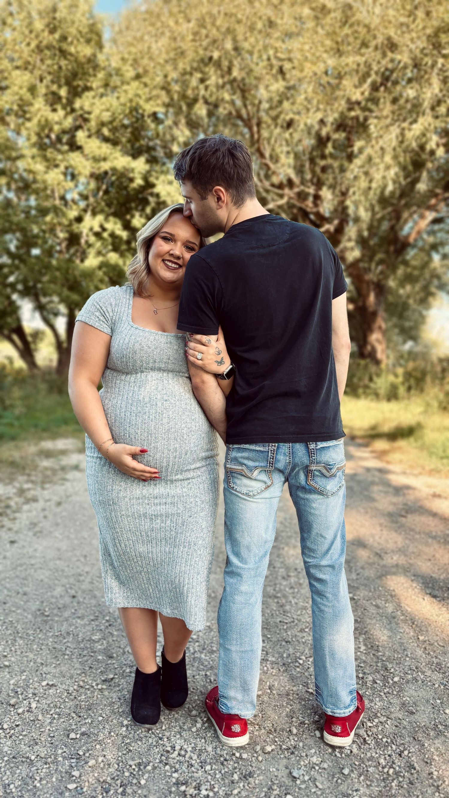 Couple during maternity session with moms hand on belly and dad kissing moms forehead.