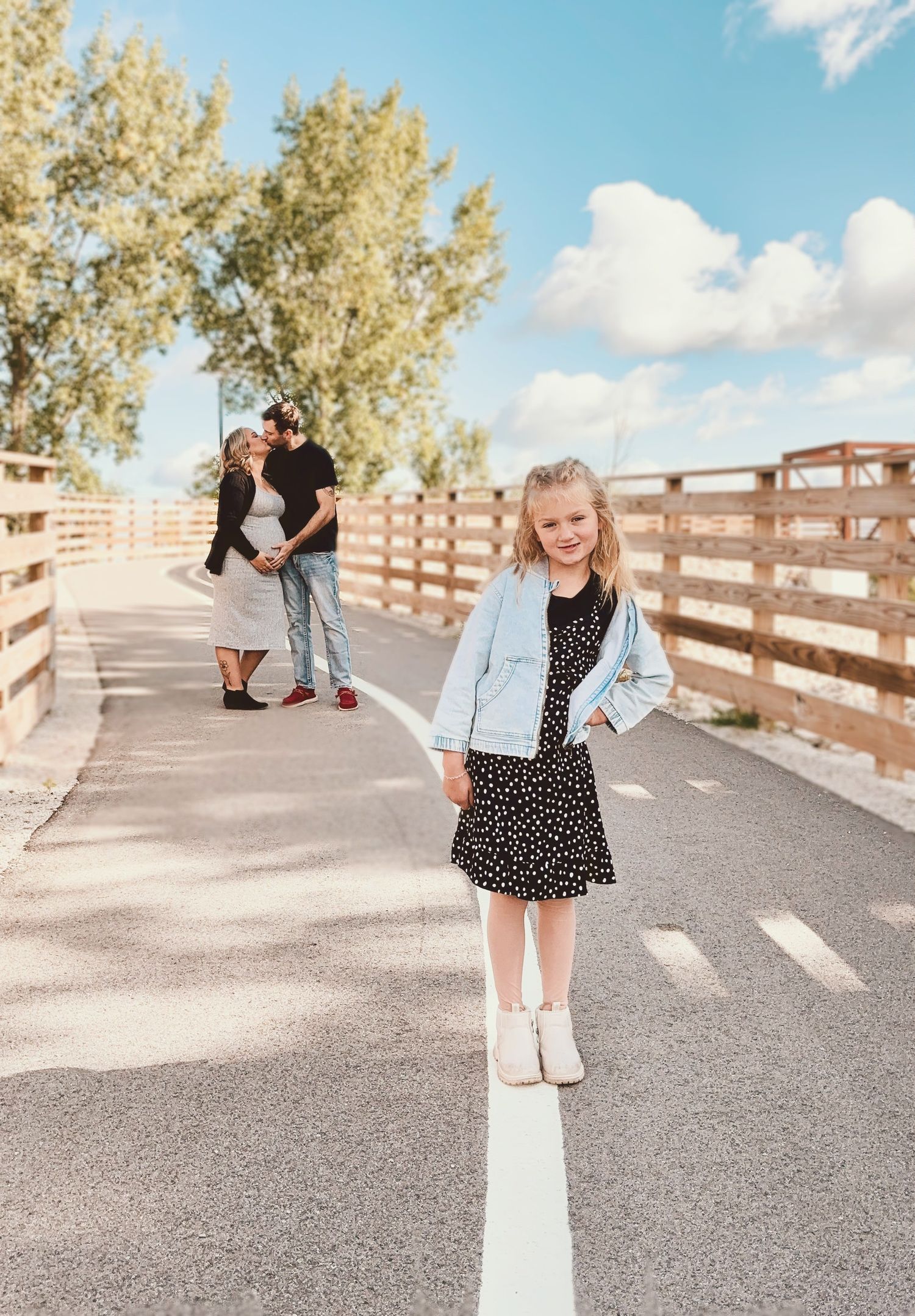 Child smiling at camera with parents kissing in background during photography session