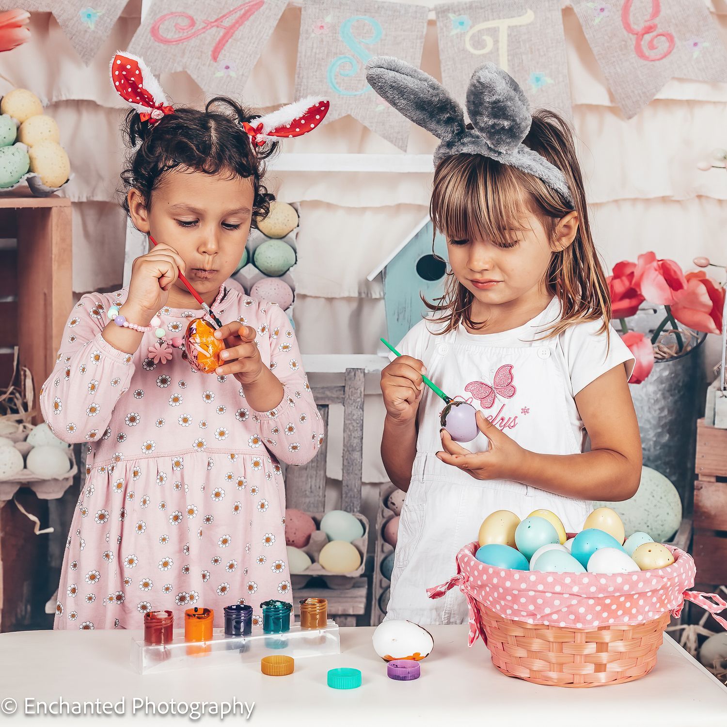 Two girls wearing bunny ears painting Easter eggs together in a colourful seasonal setup