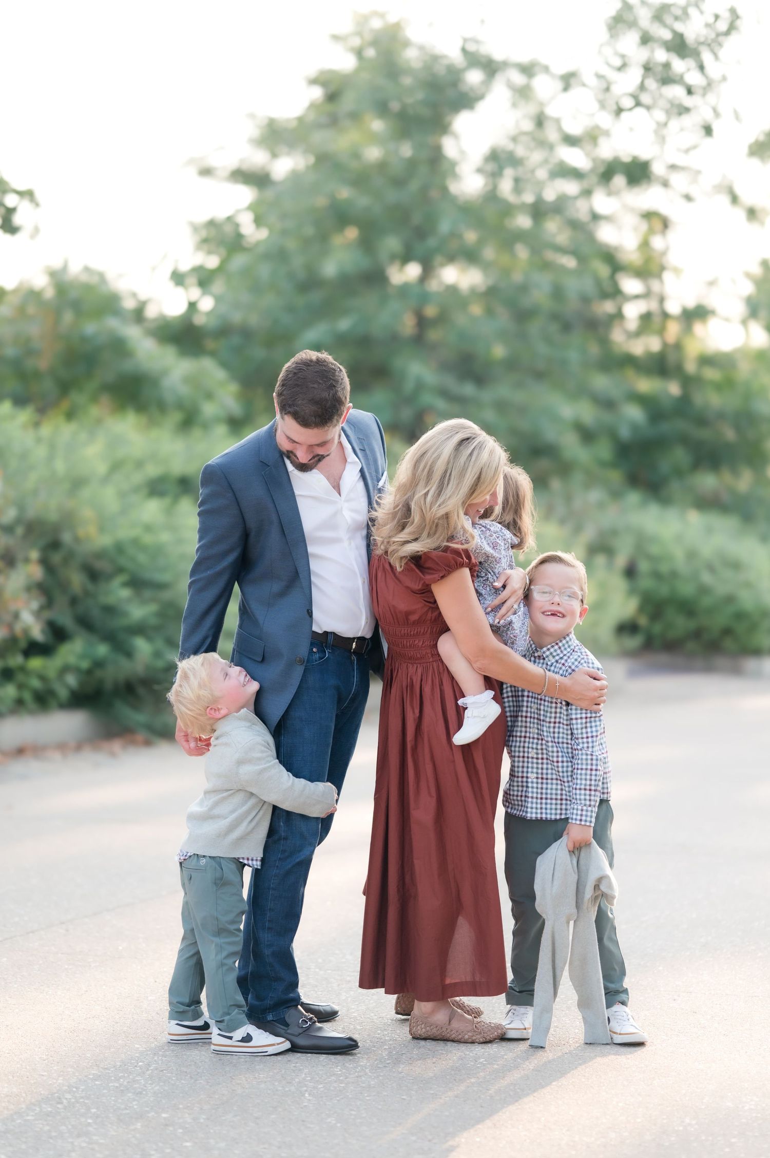 A family of five shares a joyful outdoor moment, with parents embracing three young children in casual elegant attire.