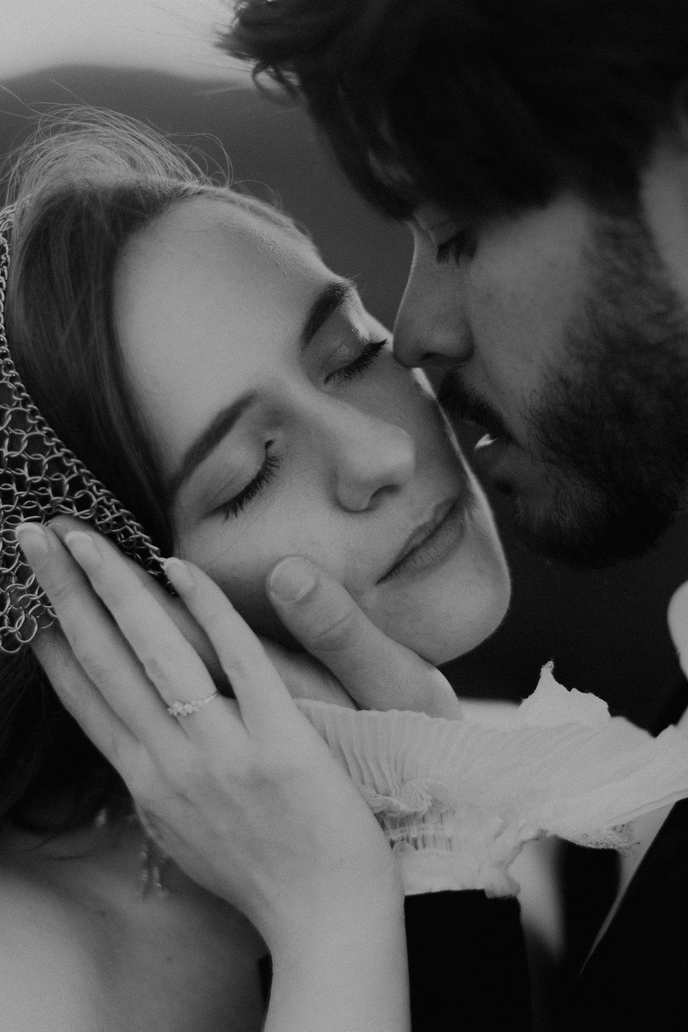 Black and white wedding photo of a groom kissing his bride's cheek as she smiles with eyes closed, wearing a veil.