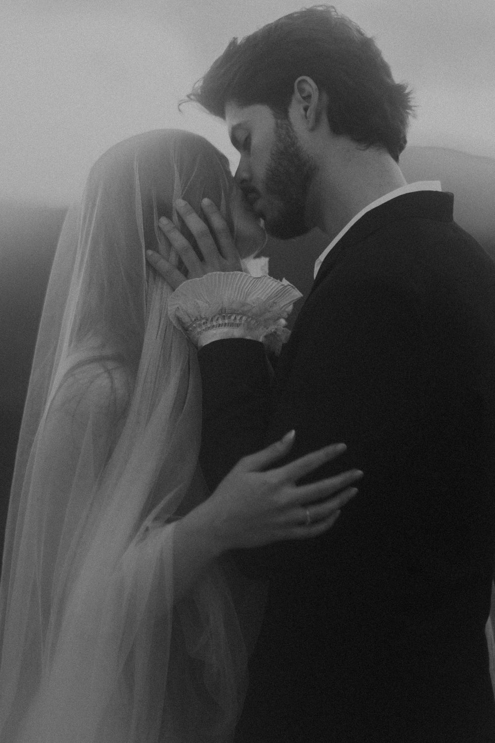 Black and white wedding photo of bride and groom sharing a kiss, bride wearing veil, groom in dark suit.