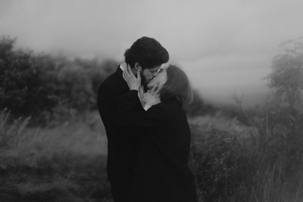 Black and white photo of a couple sharing a romantic kiss outdoors in a misty field.
