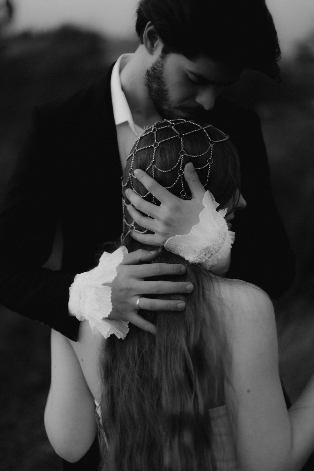 Black and white photo of a couple embracing, groom in suit hugging bride with floral accessories and long hair.