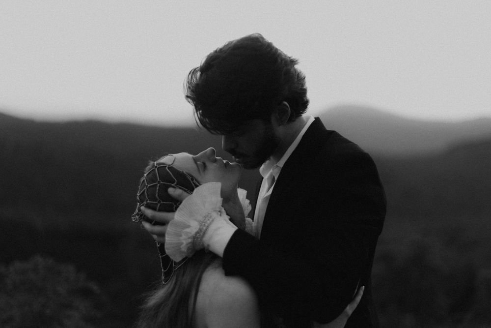 Black and white photo of a couple sharing an intimate embrace with misty mountains in the background.