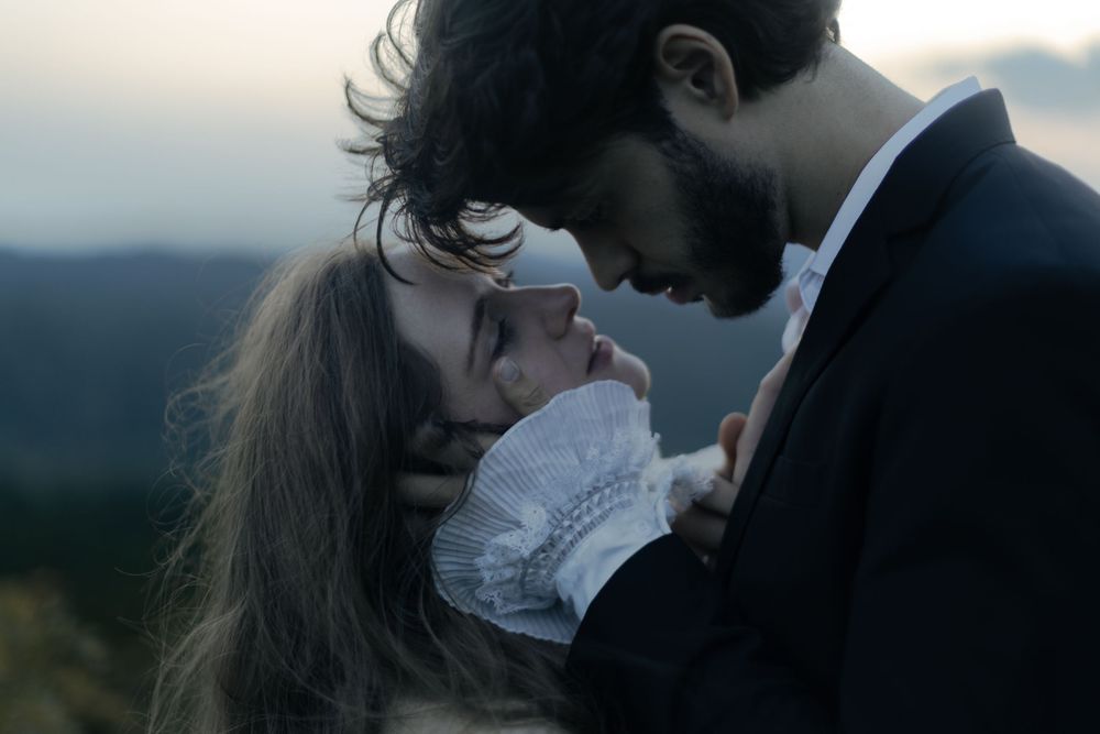A romantic couple shares an intimate moment outdoors at dusk, with the man in a suit leaning toward a woman with long hair.