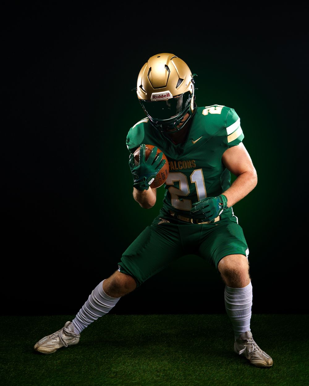 Football player in green and gold Falcons uniform #21 poses with ball in athletic stance on dark background.