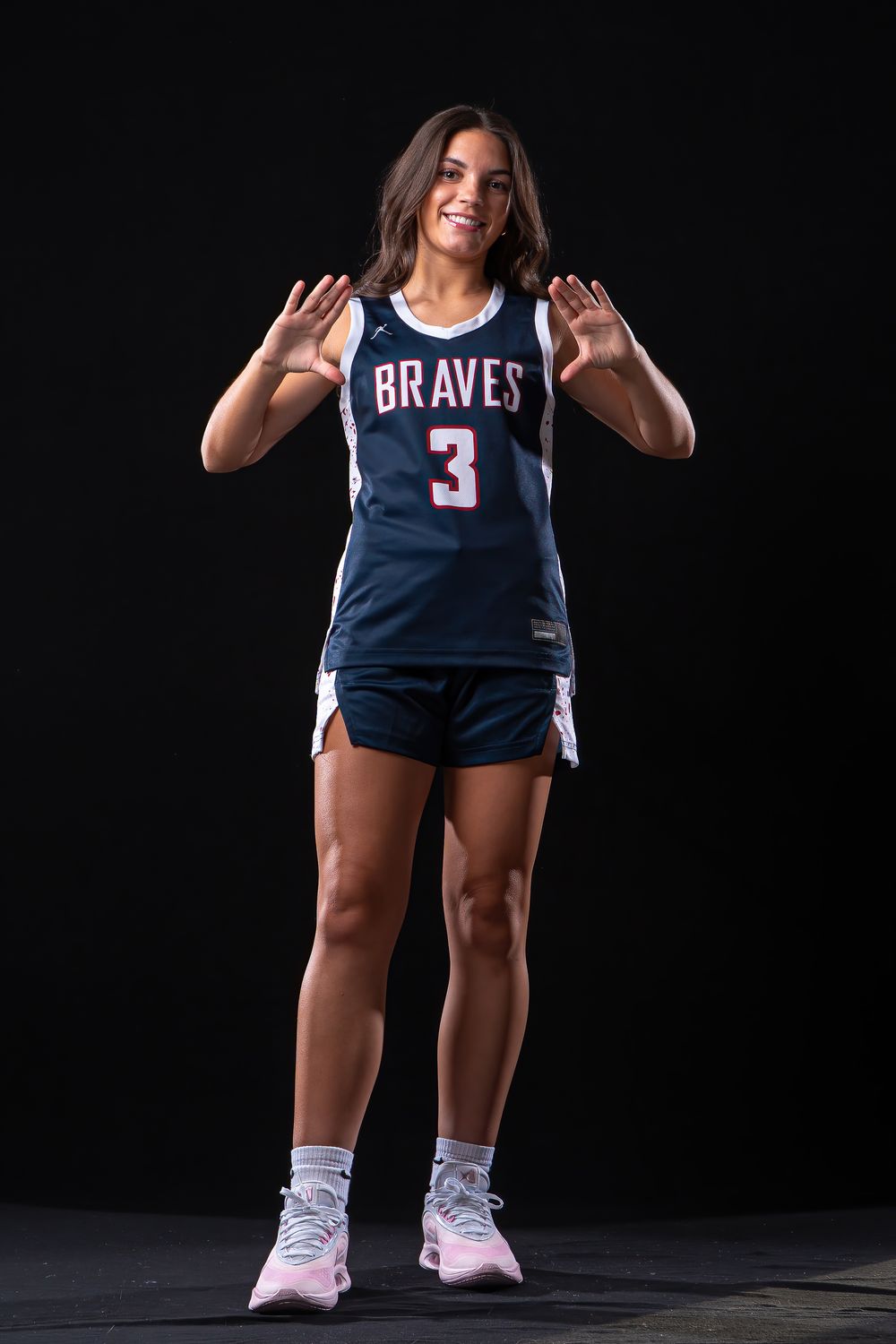 Female basketball player in Braves #3 navy jersey poses confidently against black background.