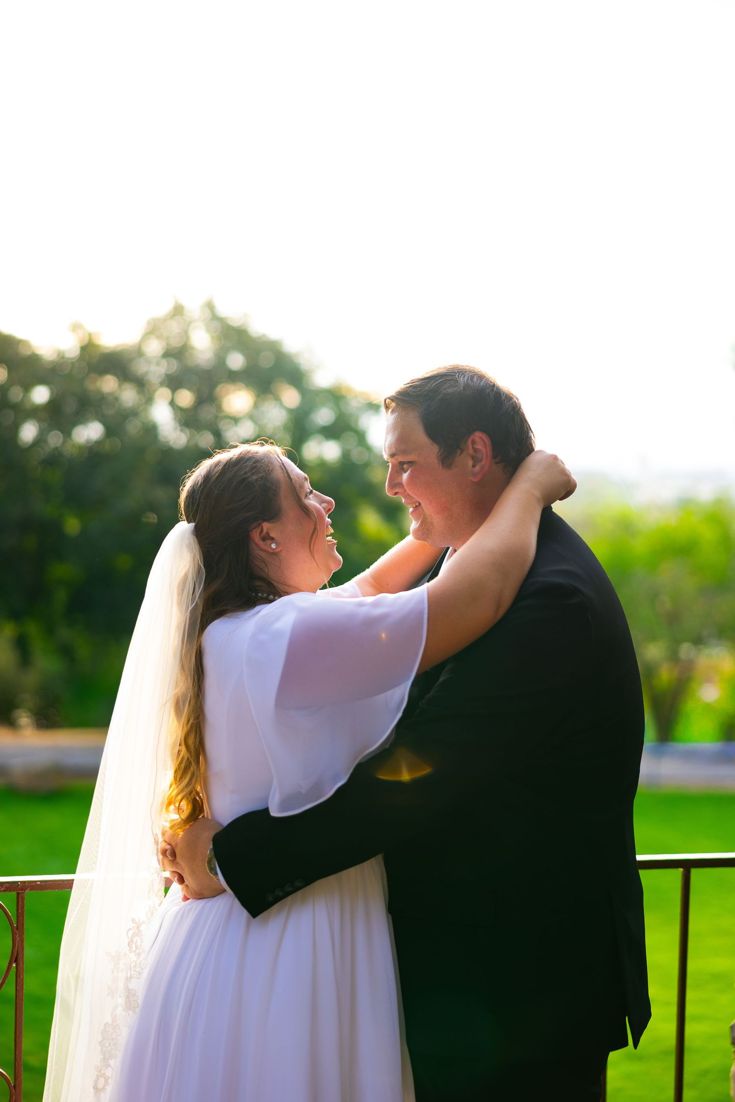 Bride in white veil and gown touching groom's face on marble steps during outdoor wedding ceremony.