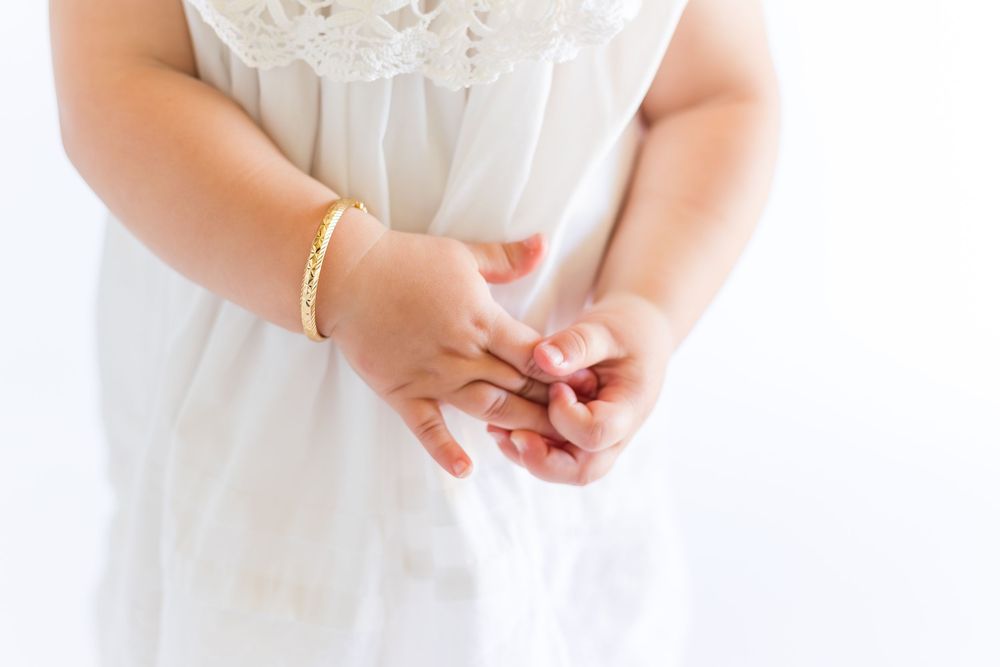 Close-up of a young child's hands gently clasped together over a delicate white heirloom dress during a classic portrait session.