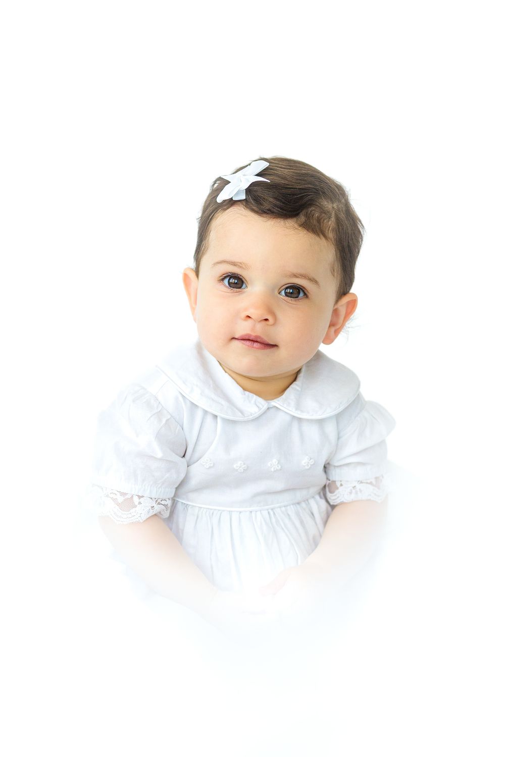 Timeless studio heirloom portrait of a young boy wearing a light blue collared outfit against a soft white background.