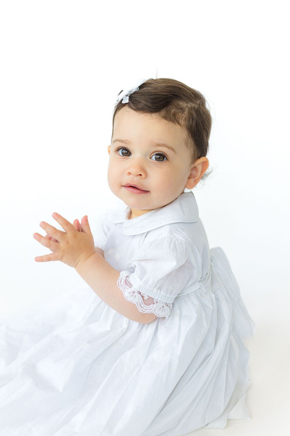 Young boy in a pale blue heirloom outfit sitting sideways and looking toward the camera against a bright white studio background.