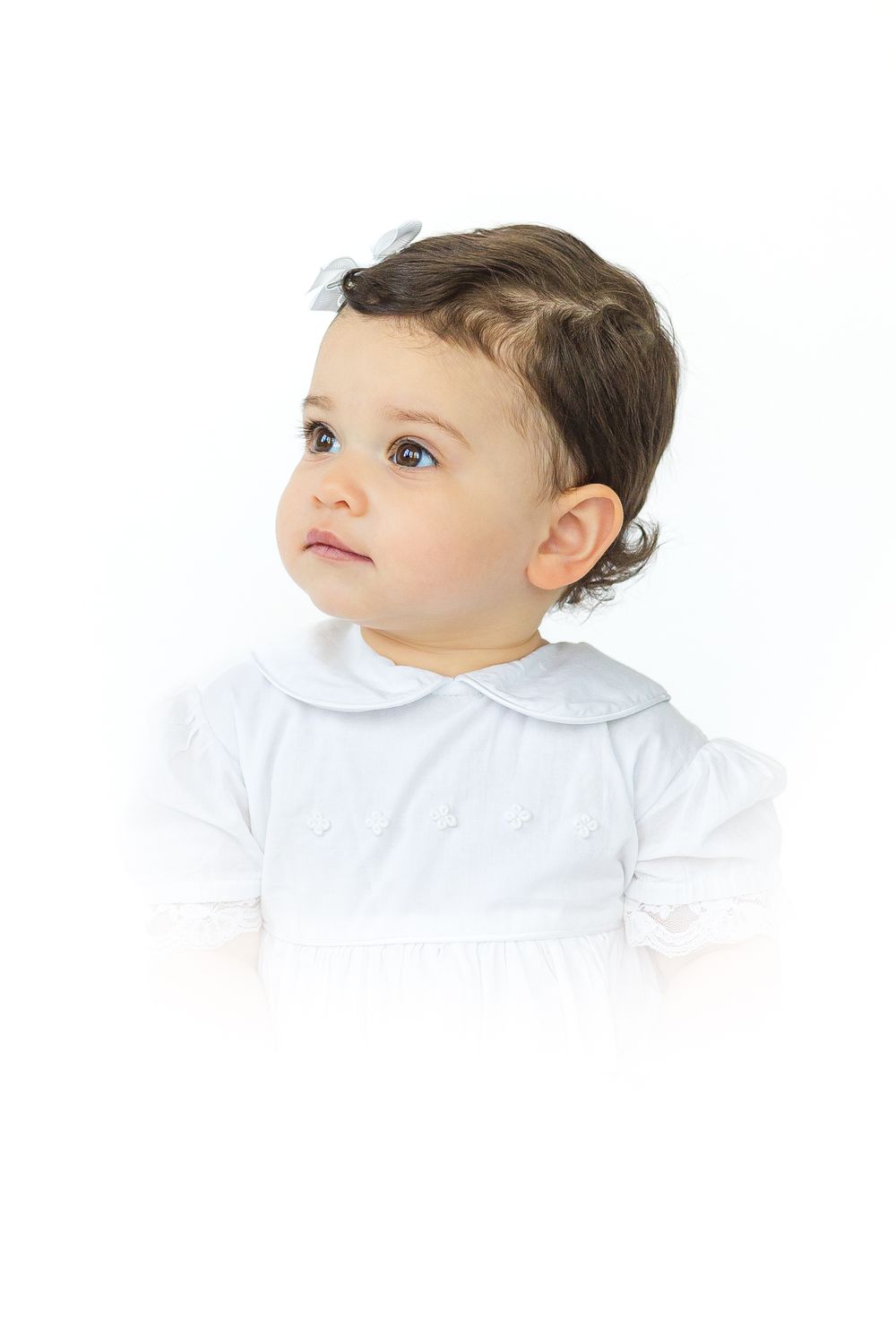 Young boy with dark hair wearing a pale blue collared outfit, looking upward during a classic children's heirloom portrait.