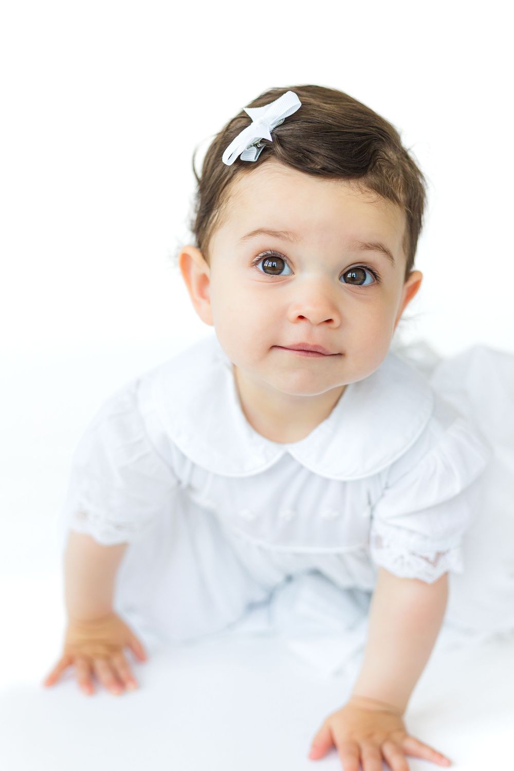 Baby boy wearing a light blue traditional outfit looking toward the camera during a timeless white-background heirloom portrait.