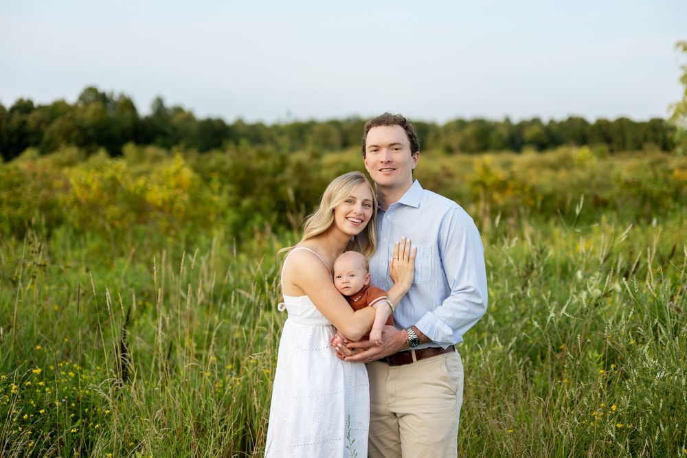 A young family with a baby poses in a lush green meadow during golden hour outdoor photography session.
